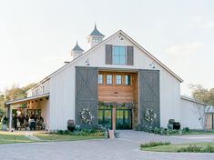 a large white barn with flowers and greenery on the front door is surrounded by people standing outside