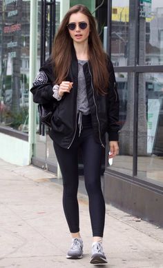 a woman in black jacket and leggings walking down the street with sunglasses on