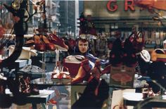 a woman sitting in a chair surrounded by lots of shoes and purses on display