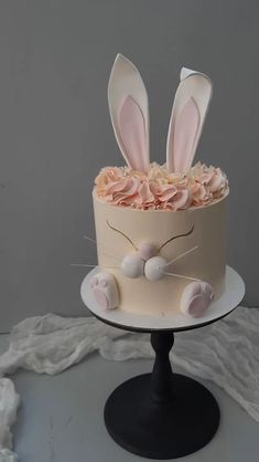 a cake decorated with pink flowers and bunny ears on a black stand against a gray background