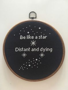 a black and white cross stitched hoop hanging on a wall with the words, be like a star distant and dying