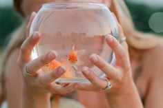 a woman holding up a fish bowl with goldfish in it and two other hands