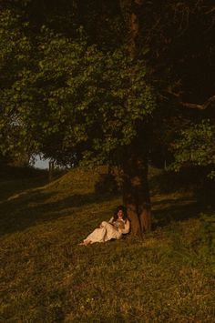 a woman laying under a tree in the grass