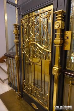 an ornate gold door with glass panels and metal bars on the sides, in front of some stairs