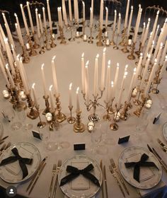 a table topped with lots of white plates and silverware next to tall lit candles