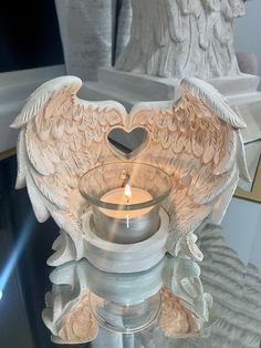 a glass candle holder with angel wings and a heart shaped candle in the center on a mirrored surface