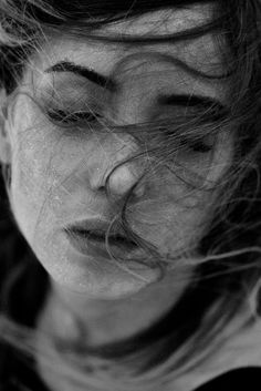 a black and white photo of a woman's face with her hair blowing in the wind