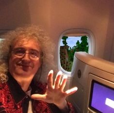 a man with curly hair and glasses holds up his hand in front of an airplane window