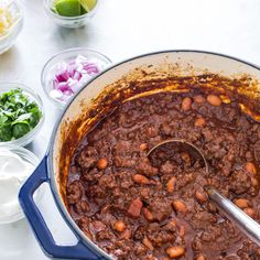 a pot filled with chili and beans on top of a table next to bowls of salad