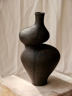 a large black vase sitting on top of a wooden table next to a white wall