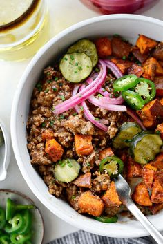 a bowl filled with meat and vegetables next to a glass of wine