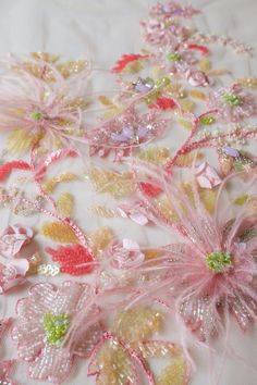 some pink and yellow flowers on a white fabric with sequins in the middle