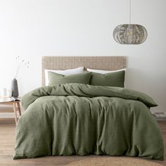 a bed with green comforter and pillows in a white room next to a table