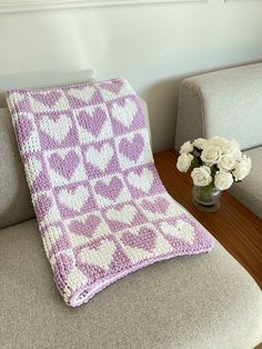 a crocheted blanket sitting on top of a couch next to a vase with flowers