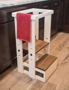 a wooden step stool with a red towel on it in the middle of a kitchen