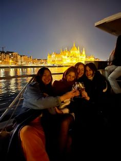 four women toasting while sitting on a boat in front of the city at night