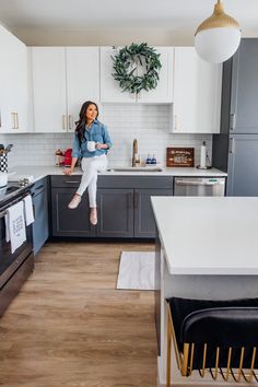 a woman jumping into the air in a kitchen with white cabinets and wood flooring