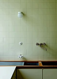 a kitchen sink and faucet in front of a green wall with white tiles