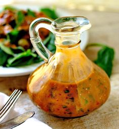 a glass carafe filled with sauce next to a plate of salad