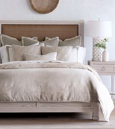 a bed with beige linens and pillows in a white room next to a clock