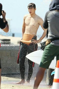 a shirtless man is standing in the water with his surfboard and cameraman