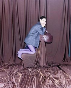 a man sitting on top of a chair in front of a curtain