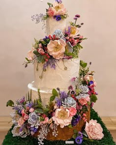 a three tiered wedding cake with flowers and greenery on the top is surrounded by moss