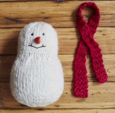 a knitted snowman ornament next to a red scarf on a wooden surface