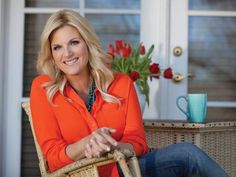 a woman in an orange shirt is sitting on a chair and smiling at the camera