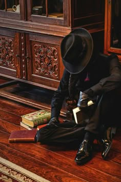 a man in a suit and hat sitting on the floor next to a bookshelf