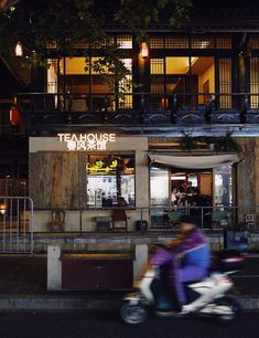 a person on a motor scooter in front of a tea house restaurant at night