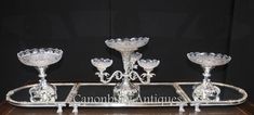 four crystal candlesticks are sitting on a glass tray with an ornate design and stand