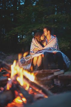 a man and woman sitting next to each other on a bench in front of a fire