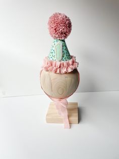 a pink pom - pom hat sitting on top of a wooden object with a ribbon around it