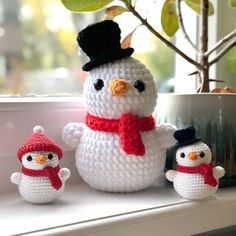 there is a crocheted snowman and two small snowmen on the window sill