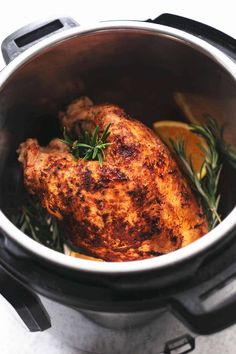 a cooked chicken in an instant pot with herbs and lemons on the side for garnish