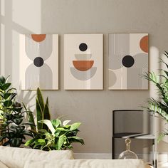 three paintings hang on the wall above a couch in a living room with potted plants