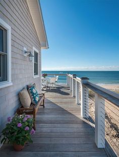 a wooden porch with chairs and flowers on the side of it next to an ocean view