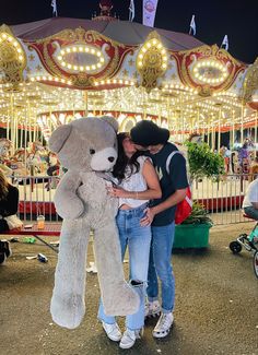 two people standing in front of a teddy bear on a merry - go - round