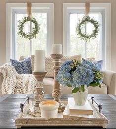 a living room filled with furniture and flowers on top of a coffee table in front of two windows