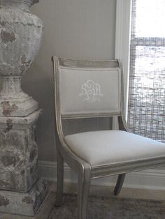 a white chair sitting in front of a window next to a tall vase on top of a table