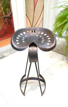 a metal stool sitting on top of a white tile floor next to a green plant