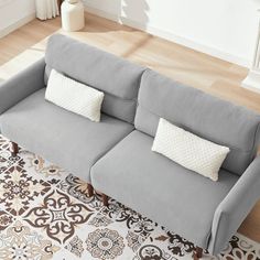 a gray couch sitting on top of a wooden floor next to a white and brown rug