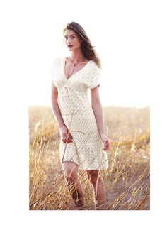 a woman in a white dress is standing in tall grass and looking at the camera