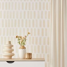 two vases with flowers sit on a table in front of a wallpapered background