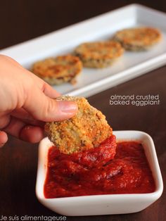 someone dipping something into a small bowl of marinara sauce on top of some fried eggplant