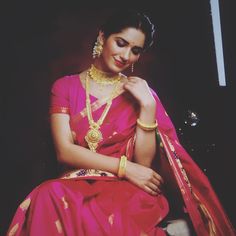 a woman in a pink sari sitting down with her hand on her chin and wearing gold jewelry