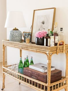 a wicker bar cart with bottles and glasses on it next to a framed photograph