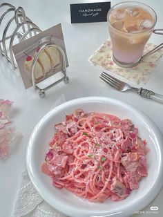 a white plate topped with pasta next to a drink