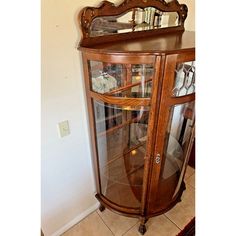 an antique wooden corner cabinet with glass doors and mirror on the top, in front of a white wall